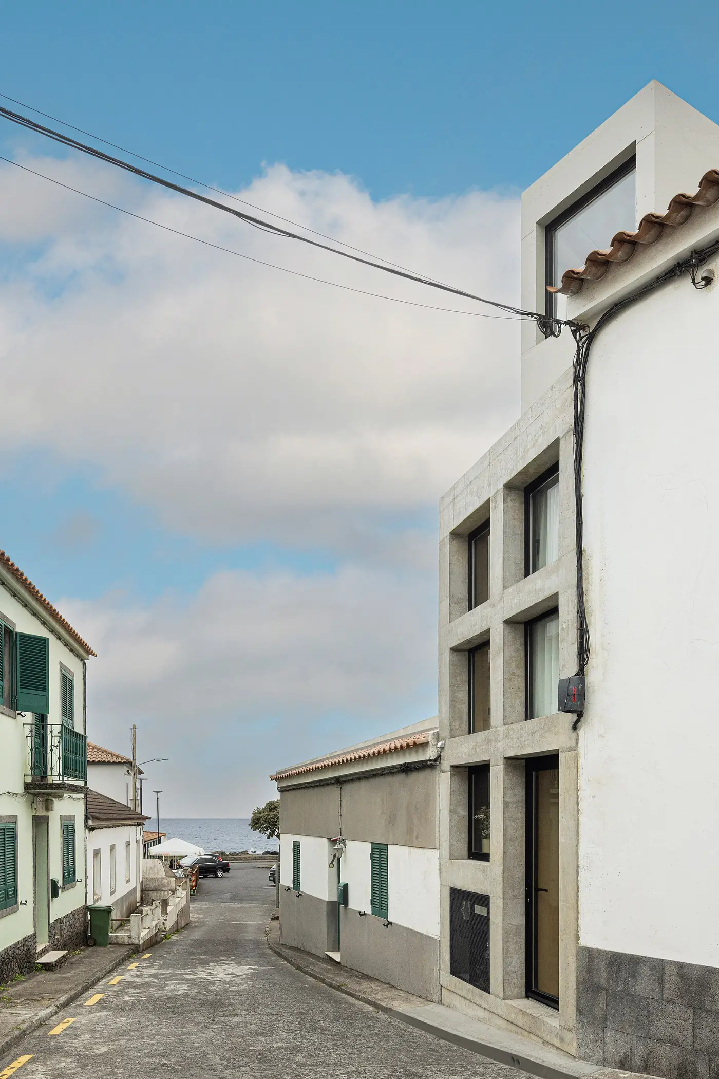 A concrete house by SO Arquitetos on a village street running down to the sea